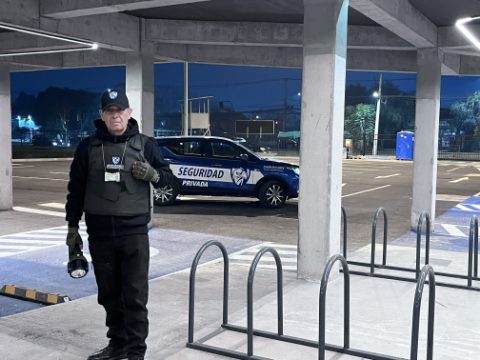 Guardia de ASCOR Security con chaleco, credencial y linterna, con el vehículo institucional detrás